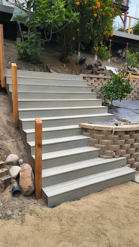 Newly built concrete staircase with wooden handrails in a landscaped yard.