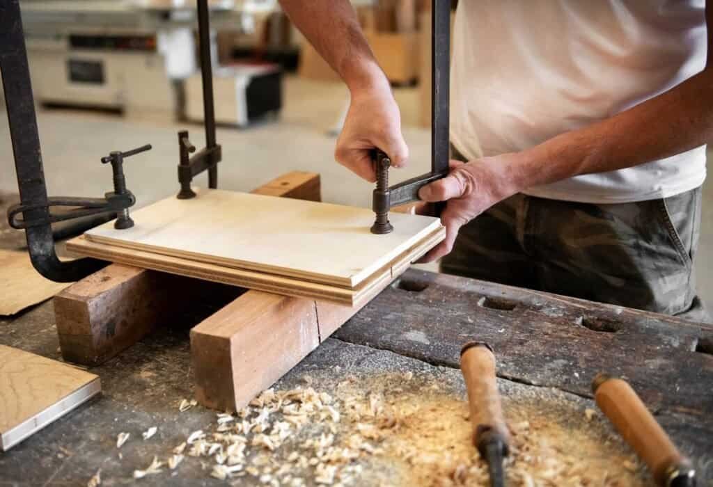 Carpenter assembling wooden panel with clamps in workshop.
