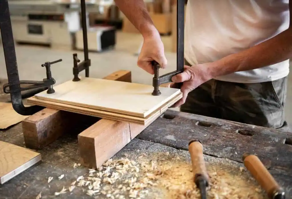 Carpenter assembling wooden panel with clamps in workshop.
